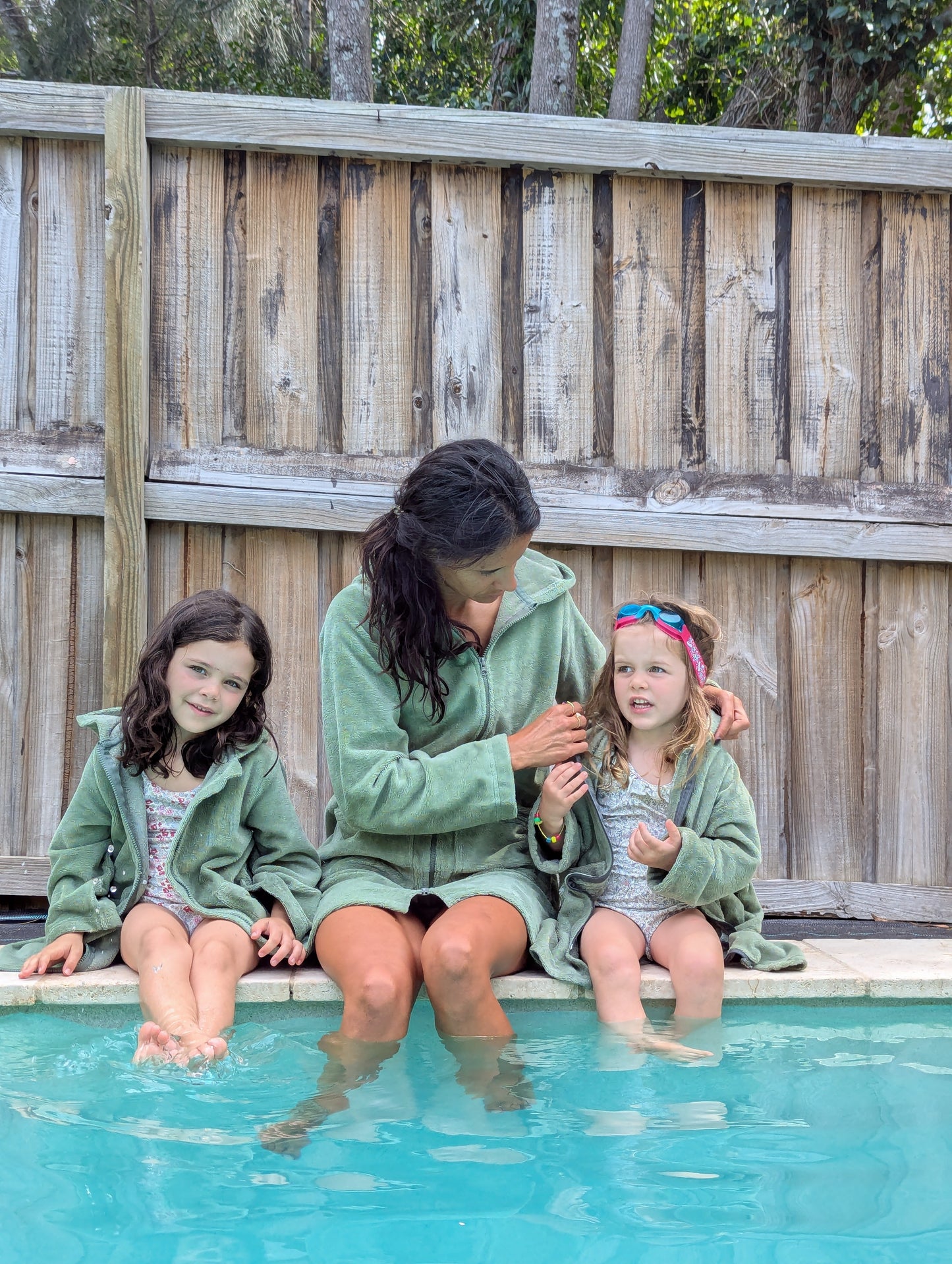 Toddlers wearing cactus hooded towels by the swimming pool with their mother.