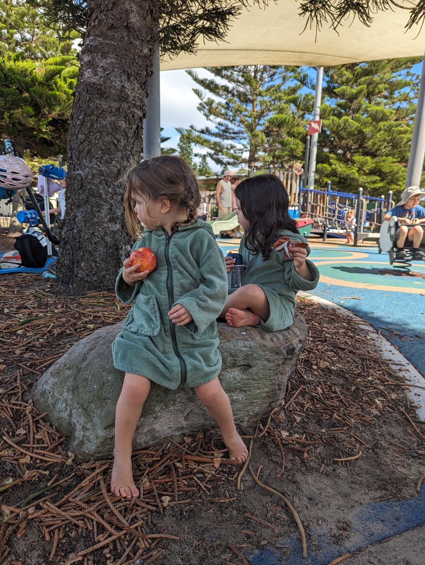 Toddlers wearing cactus hooded towels at the playground while eating snacks.