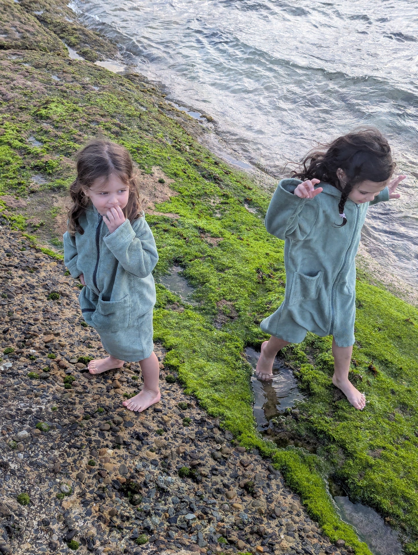 Toddlers wearing cactus hooded towels by the beach.