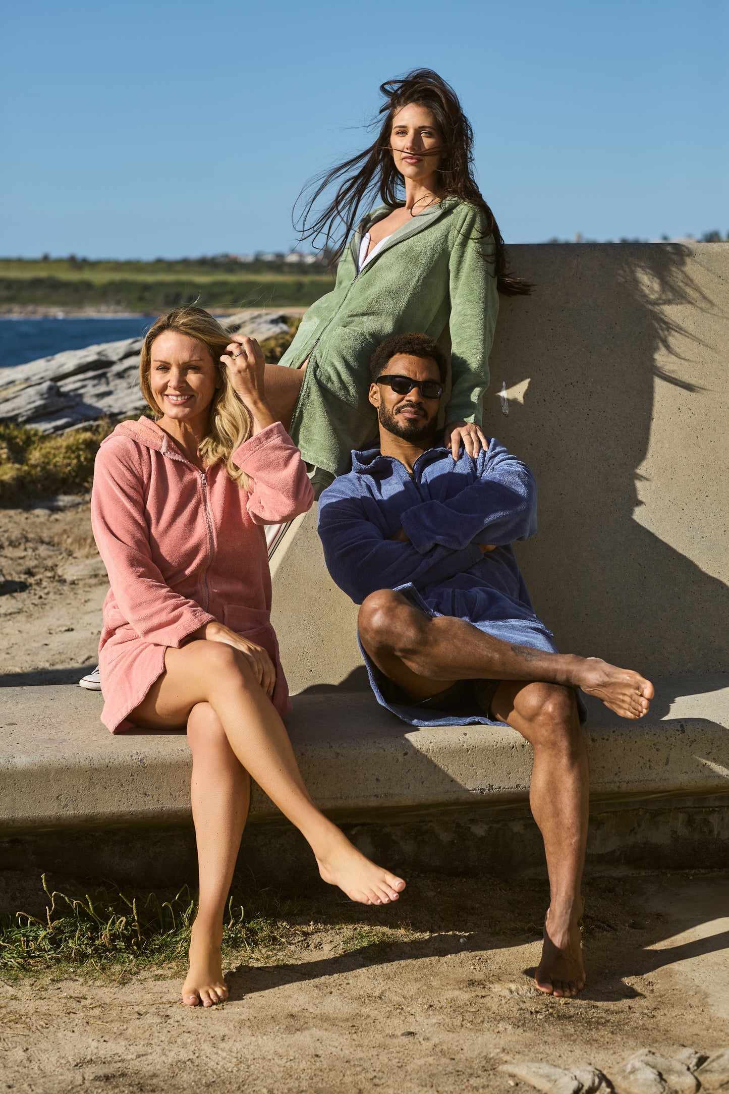 A man and two women wearing Capimiri ponchos, in cactus, guava and deep blue colors, by the beach.