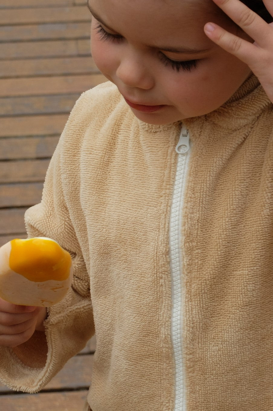Toddler wearing a Sandcastle hooded towel from Capimiri brand and eating a mango ice cream.