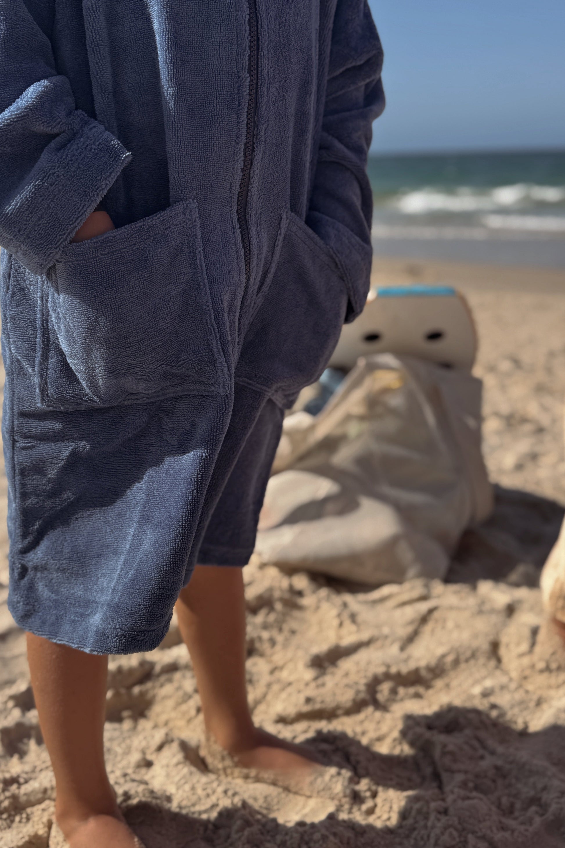 Toddler wearing a blue robe on a sandy beach with ocean waves in the background