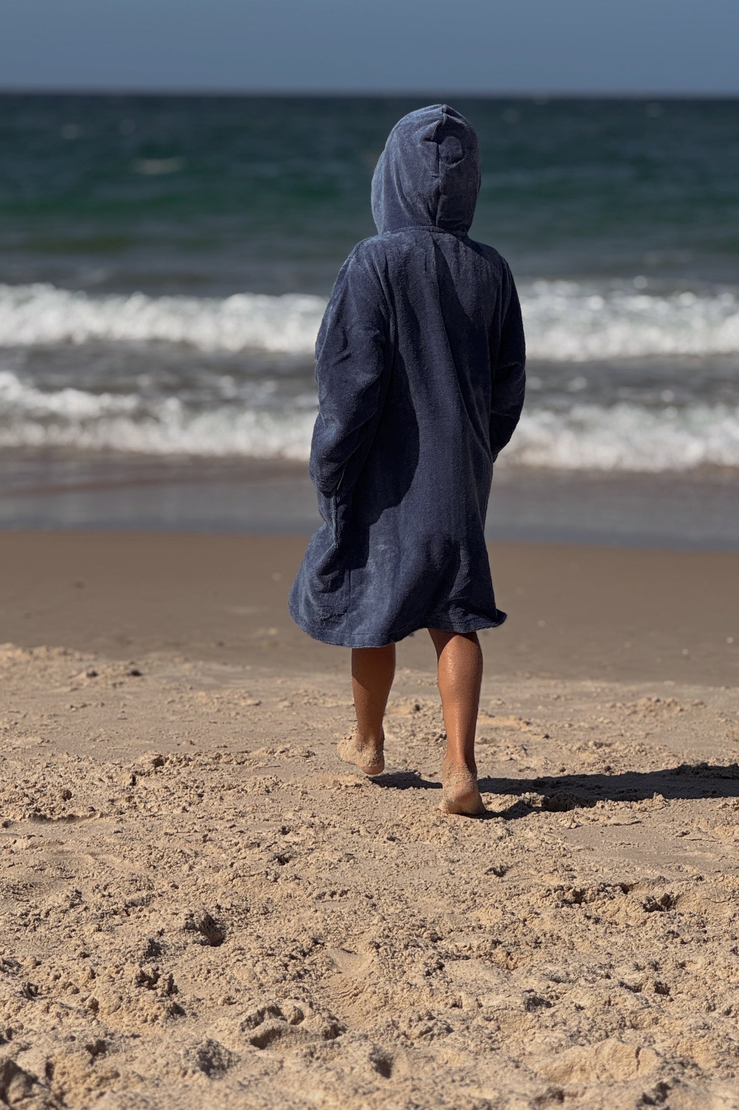 Person wearing a hooded poncho on a beach with ocean waves in the background