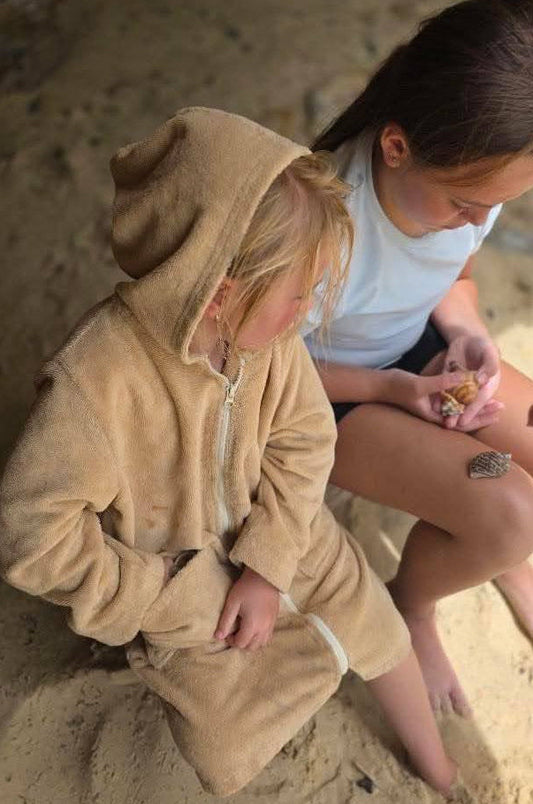 Two people sitting on a sandy surface, one in a beige hoodie and the other in a white shirt.