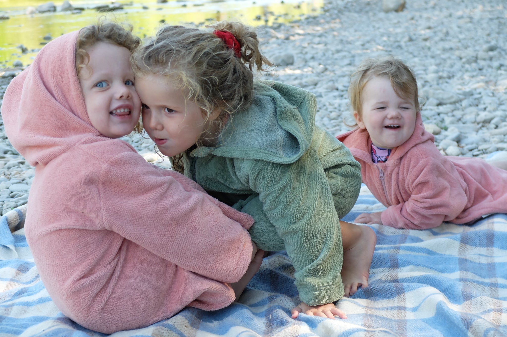 Three children in colorful outfits sitting on a blanket outdoors.